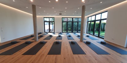 Yogakurs - vorhandenes Yogazubehör: Meditationshocker - Teutoburger Wald - Unser modernes Yoga Studio in Salzkotten wurde dieses Jahr 2021 fertiggestellt und eröffnet. In unseren großzügig und elegant gestalteten Räumen fühlst Du dich sofort wohl und kannst dich ganz auf dein Yoga konzentrieren. Der 100m² große Kursraum bietet auf dem Eichendielenboden Platz für +25 Yogamatten und verfügt über Sicherungspunkte an der Decke um Gurt- und TRX Bänder, Trainingsequipment und Aerial Yoga Tücher sicher anzubringen. Die optimierte Ton- und Lichttechnik, schaffen eine ganz besondere Atmosphäre in den Yogastunden. Die angenehme Wärme der Fußbodenheizung sorgt in der kalten Jahreszeit für ein wohliges Gefühl in den Yogastunden und unterstützt dich in der Tiefenentspannung. Wenn Du dann beim Yoga mal so richtig ins Schwitzen kommst, lassen die großen Schallschutz Fensterflächen reichlich frische Luft und neuen Sauerstoff in den Raum, so lässt sich die Raumtemperatur ganz auf die Bedürfnisse der Yogastunde abstimmen. 
Unser athletic yoga Studio ist mit den hochwertigen 6mm dicken Kurma Black Grip Yogamatten in gr. L ausgestattet. Diese bieten mit einer Mattenfläche von 200x60cm ausreichend Platz für deine Yogaübungen und die Tiefenentspannung, selbst wenn Du etwas größer bist. Neben Sitzkissen, Decken und Gurtbändern gibt es Korkblöcke, Kopfstandständer und allerhand anderes Equipment, das dir in der Yogastunde zur Verfügung steht. 
 - Marlon Jonat | Athletic Yoga in Salzkotten